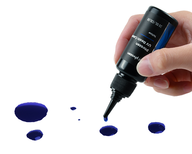 Hand squeezing a Phrozen blue UV resin colorant bottle, with drops of blue colorant on a white surface.